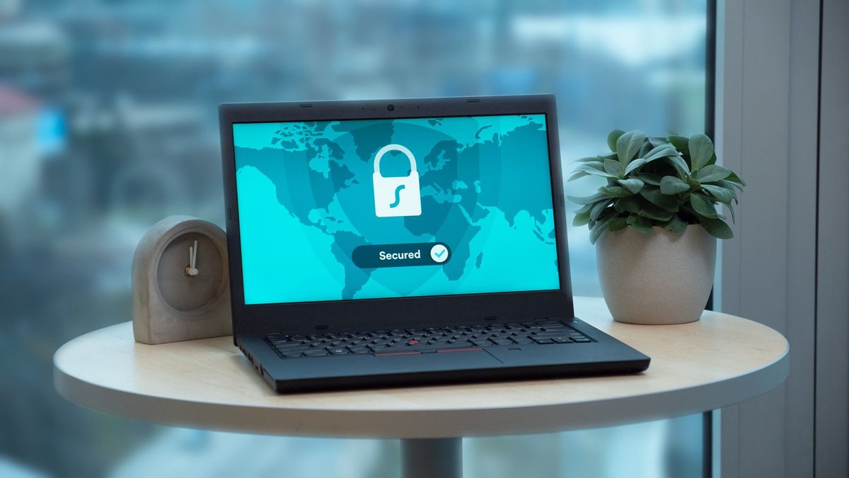 Notebook exibindo tela de segurança com cadeado, sobre mesa com planta