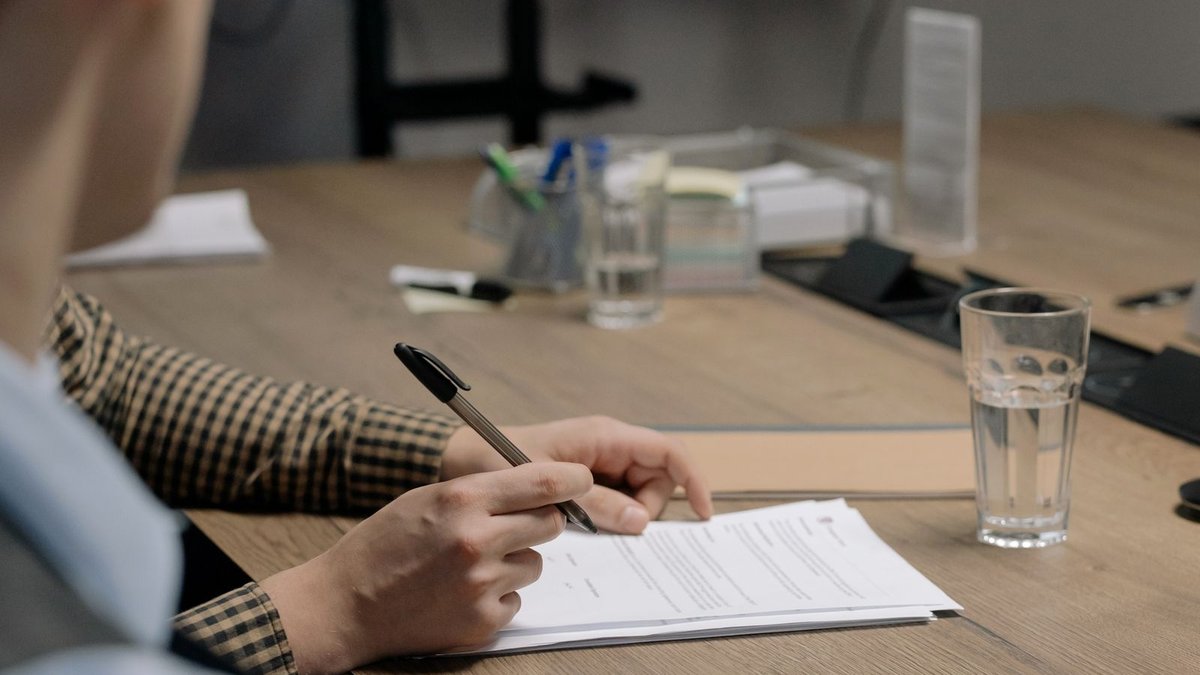 Pessoa assinando e revisando documento sobre a mesa